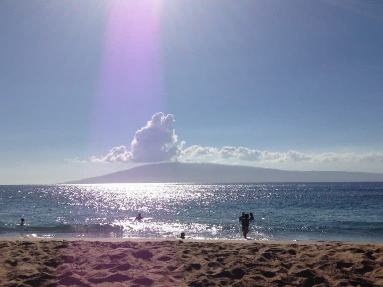 Bright sunlight over a beach with shimmering sea and distant island, highlighting outdoor lighting and solar energy.