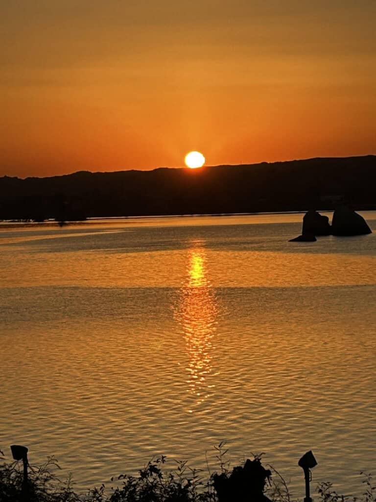 Vibrant sunset over water with silhouettes, highlighting lighting and outdoor ambience.