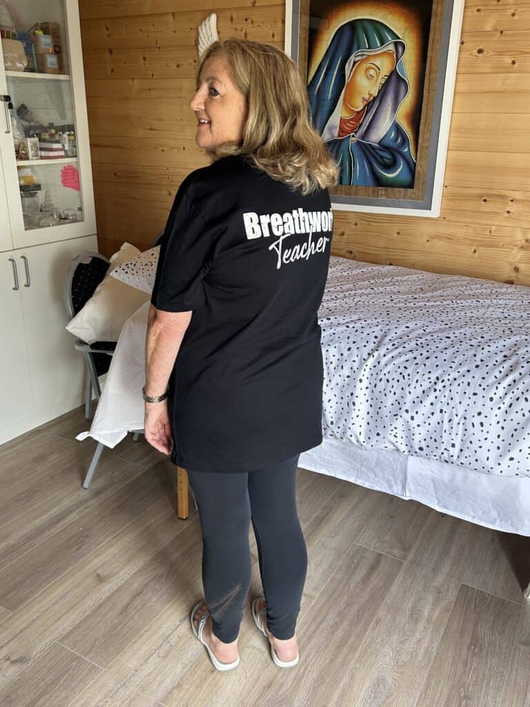 Comfortable woman wearing a "Breathwork Teacher" t-shirt, preparing for a session in a cosy room.