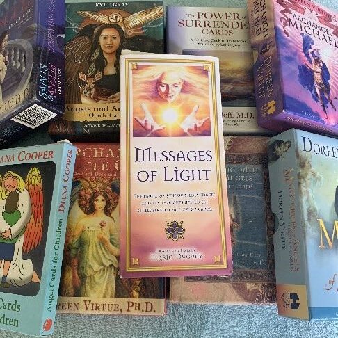 A set of spiritual and angel oracle cards on a table, including "Messages of Light" and other mystical decks.