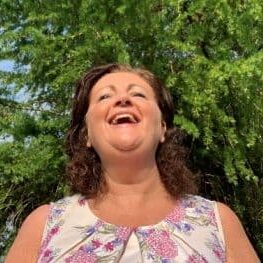 Bright woman smiling outdoors with greenery in background, promoting lighting and illumination solutions.