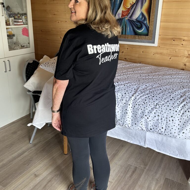 Comfortable woman wearing a "Breathwork Teacher" t-shirt, preparing for a session in a cosy room.